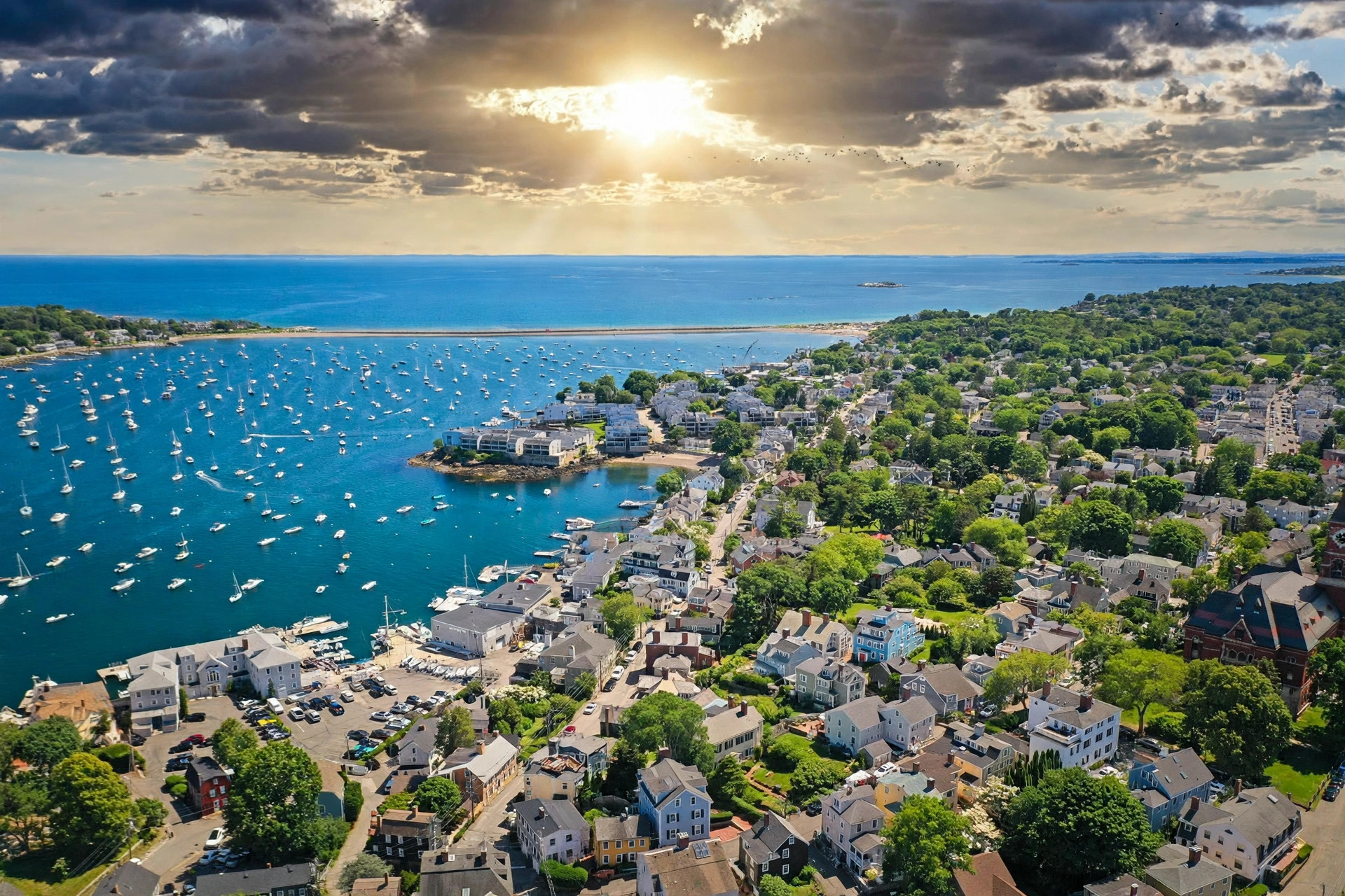 Marblehead Harbor at golden hour, sailboats anchored below historic shingle homes